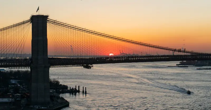 Scenic view of the Brooklyn Bridge with a vibrant sunset over New York City's skyline.