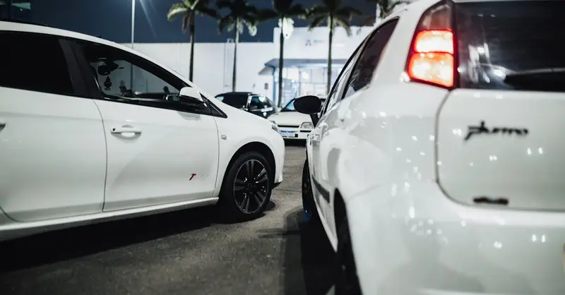 White cars gathered at a nighttime car meet in an illuminated parking lot.
