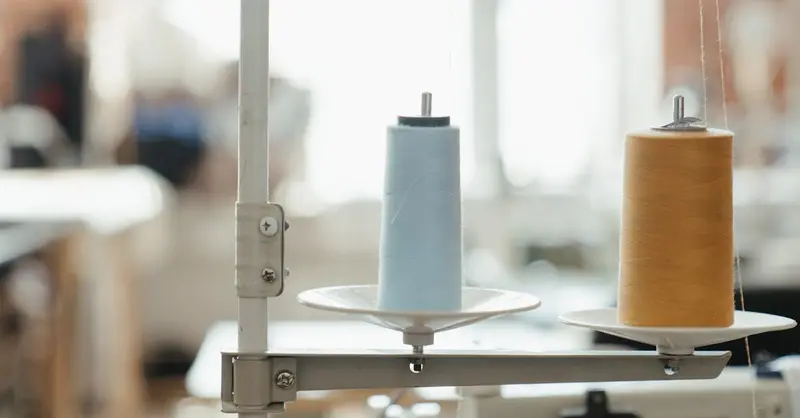 Close-up of blue and yellow thread spools on a sewing machine, lit by soft natural light.