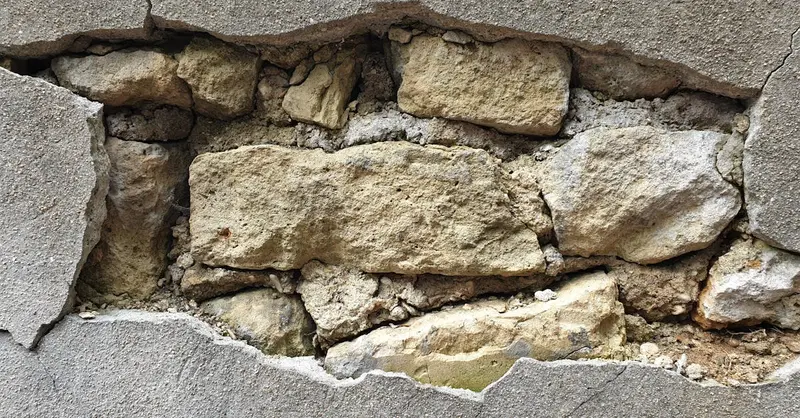 Detailed view of a cracked concrete wall exposing the underlying stonework and texture.