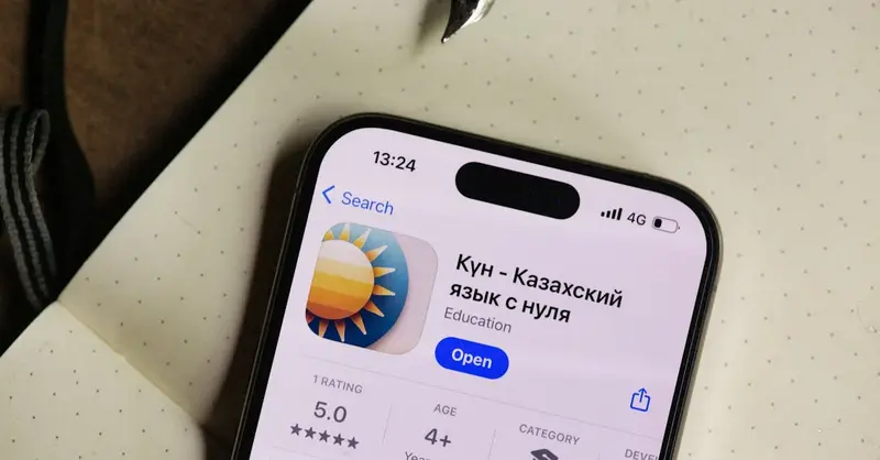 Close-up of a smartphone screen showing a Kazakh language learning app in an open notebook setting.