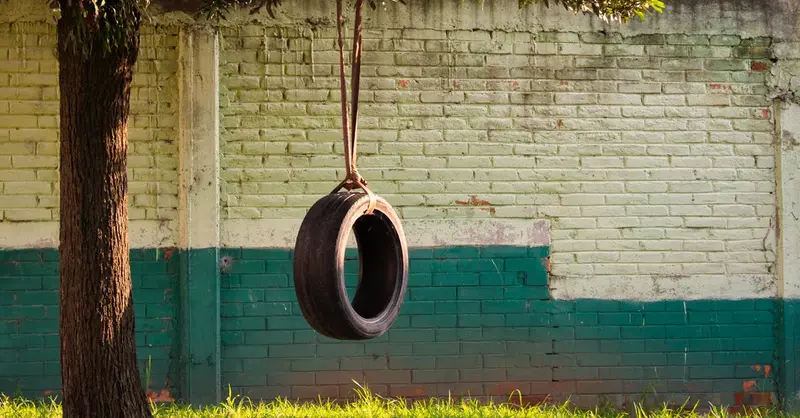 A nostalgic tire swing hanging from a tree, next to a brick wall in Lerma de Villada, Mexico.