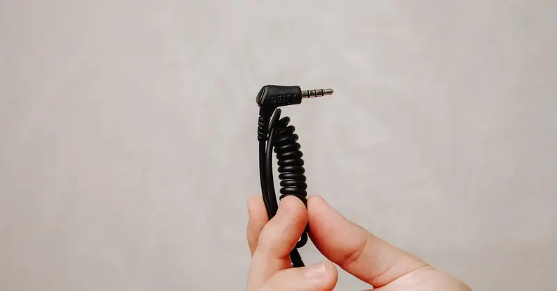Closeup of a hand holding a coiled audio cable plug against a neutral background.