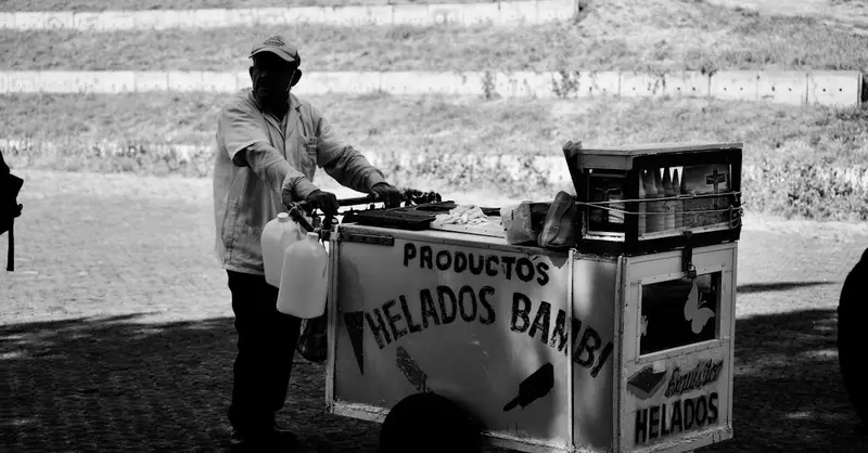 Monochrome image of a traditional ice cream vendor with a classic cart on a street.