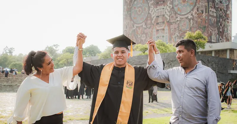 Happy graduate celebrating with parents at UNAM library in Mexico City.