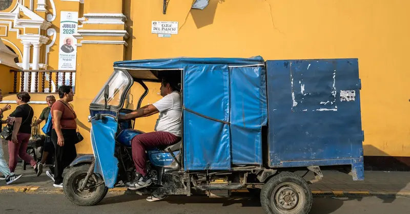 A vibrant blue tuk-tuk driving past a colonial building in Trujillo, Peru.