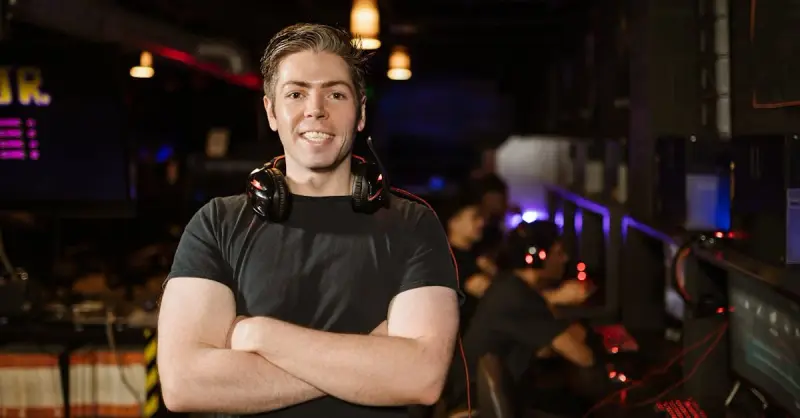 Smiling gamer standing with headphones in an illuminated gaming arena.