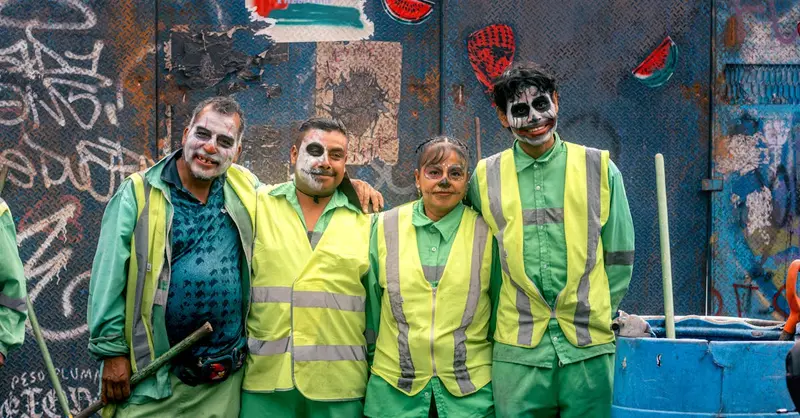 Group of people in Catrina makeup celebrating Day of the Dead in front of urban graffiti.