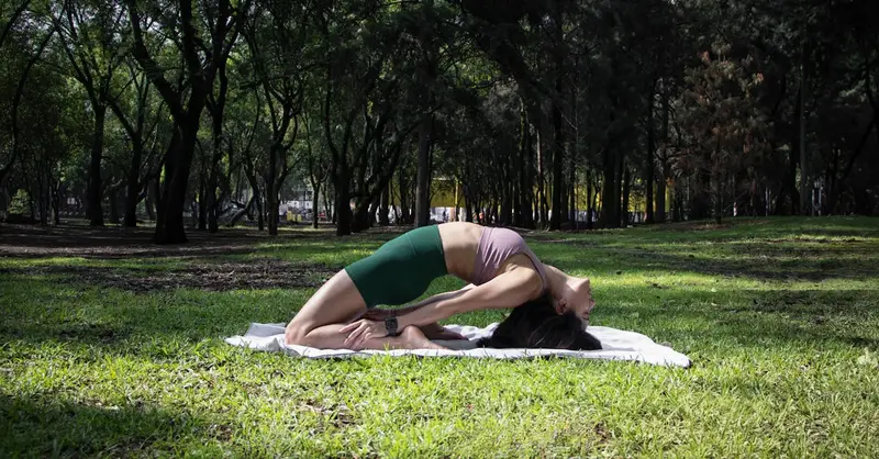 Woman performing a yoga pose on a sunny day in a lush green park in Ciudad de México.