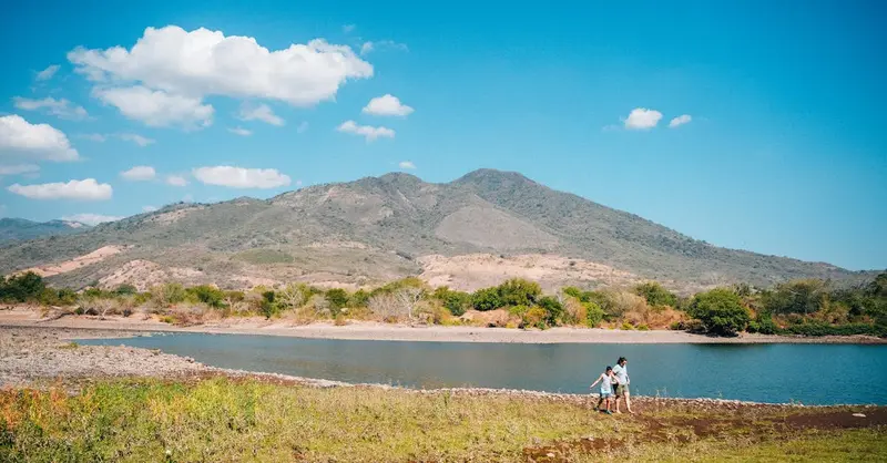 Scenic view of hikers by a lake with stunning mountain backdrop in El Salvador, perfect for outdoor adventures.