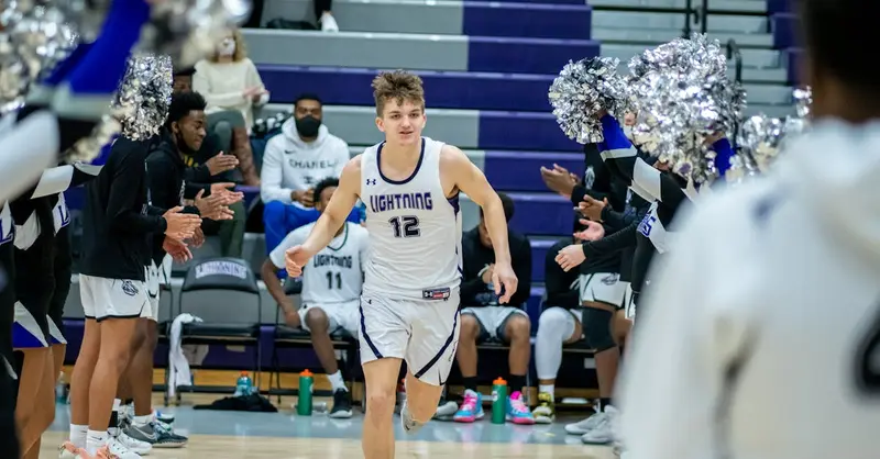 Young basketball player enters court surrounded by cheering teammates and fans.