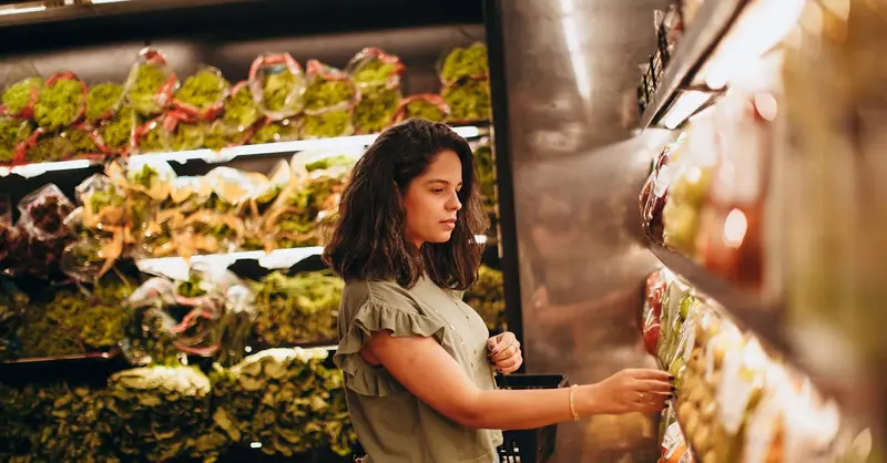 Young woman selecting fresh vegetables in a supermarket produce aisle.
