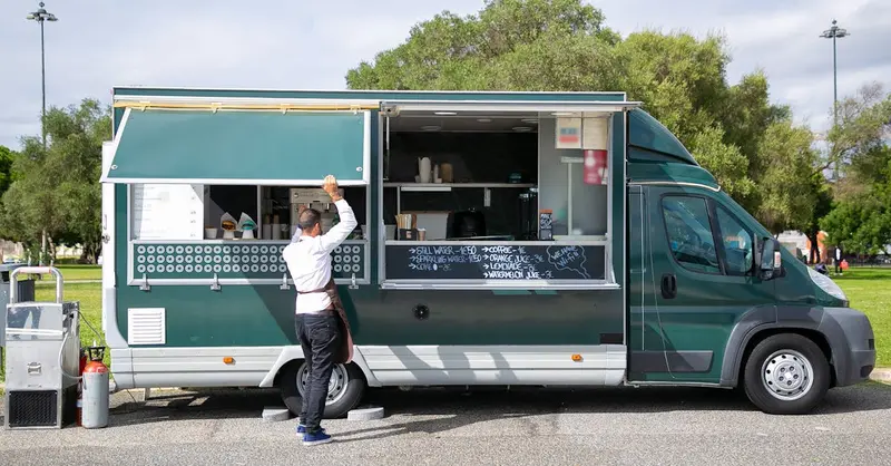 Back view full body of anonymous male worker opening windows of car with street food parked in park