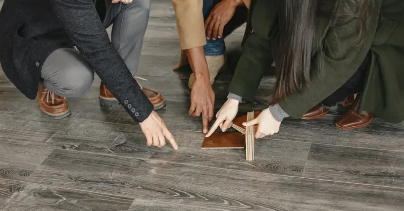 Three adults selecting flooring options indoors, focused on wooden samples and decision-making.