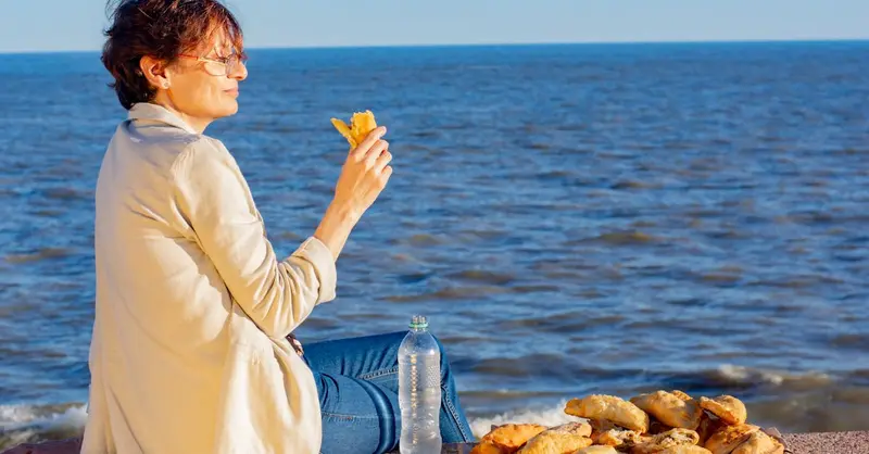 A woman enjoys empanadas by the ocean in Montevideo, Uruguay during a sunny day.