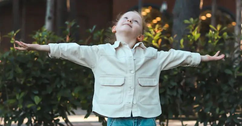 Child embracing nature with open arms in a serene outdoor setting.