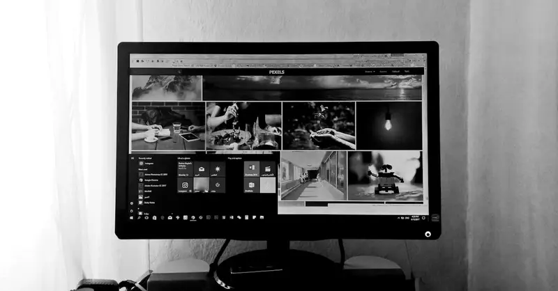 A black and white photo of a computer monitor displaying various images and applications in an indoor setting.