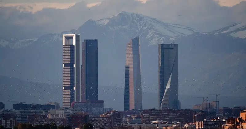 View of Madrid's skyline featuring Cuatro Torres against a backdrop of mountains.
