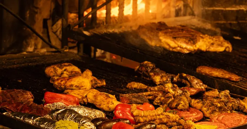 A variety of meats and vegetables cooking on an open grill, typical of Montevideo's traditional asado.