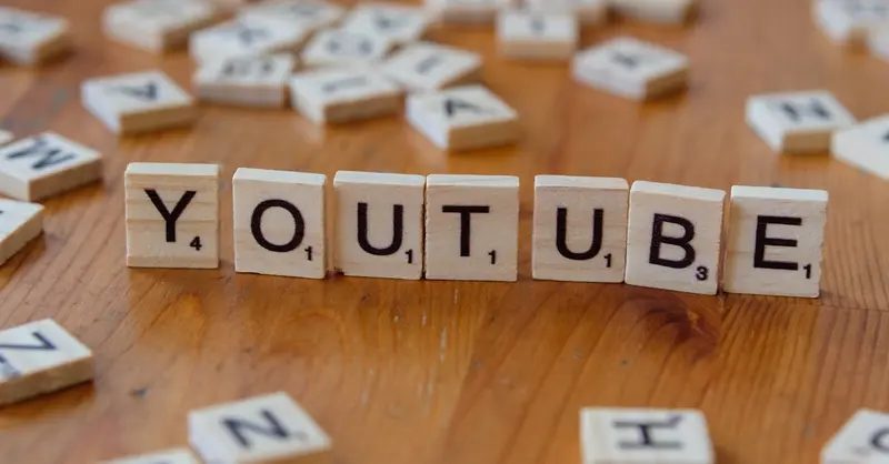 Wooden letter tiles spelling 'YOUTUBE' on a wooden surface, symbolizing video sharing and streaming.