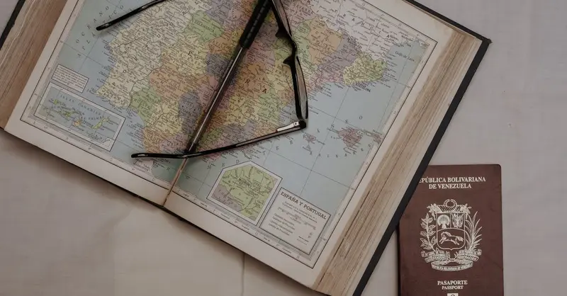 A vintage map of Spain with eyeglasses and a Venezuelan passport, symbolizing travel planning.