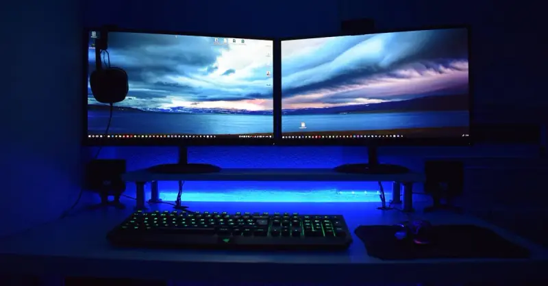 Dual monitors with blue lighting on a gaming desk setup.