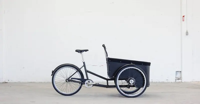Side view of a three-wheeled cargo bike in a minimalistic indoor setting.