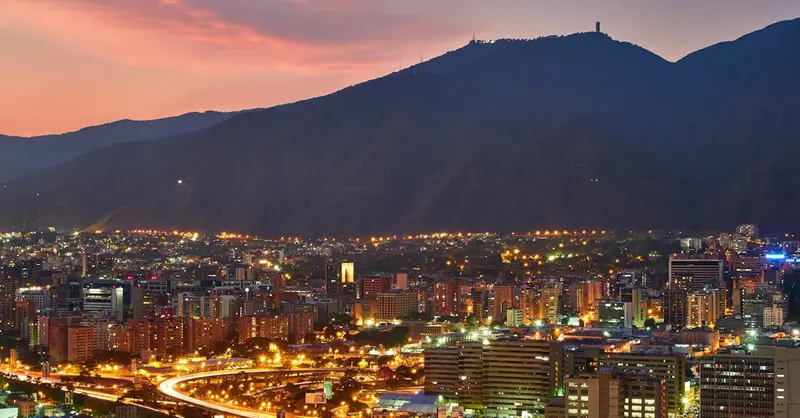 A stunning aerial view of Caracas cityscape at dusk, showcasing the vibrant city lights against the mountainous backdrop.