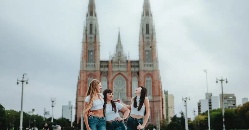 Three women share a joyful moment in front of the iconic La Plata Cathedral, Argentina.