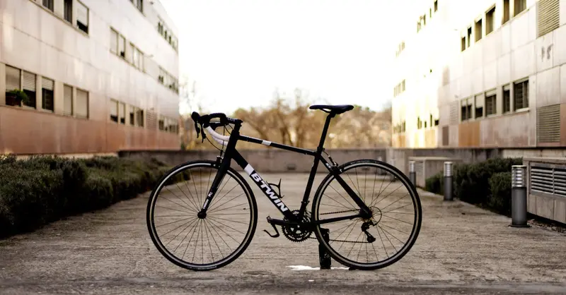 A black bicycle parked between modern buildings on an urban road.
