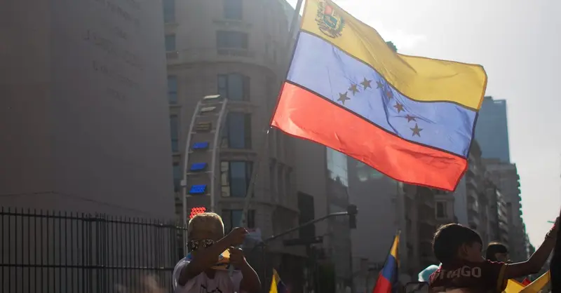 Venezuelans gather, waving national flag in city protest for freedom and change.