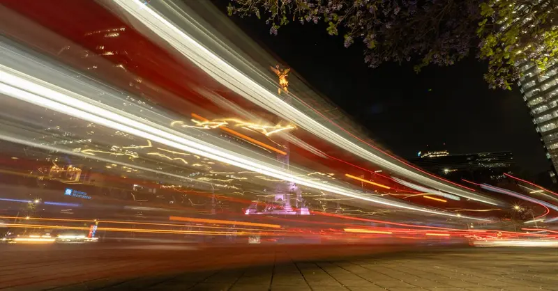 Vivid light trails surround the Angel of Independence in bustling Mexico City at night.